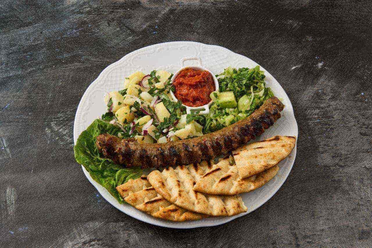 Balkan-Wurst Hausgemachte Balkan-Wurst mit Ajvar, Kartoffelsalat, frischem Gurkensalat und Fladenbrot – traditionelles Essen zum Mitnehmen
