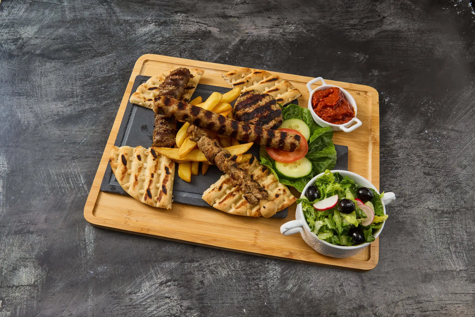 Grillplatte Balkan-Grillplatte mit Cevapcici, Schweinefiletspieß, Grillwurst, Fladenbrot, Pommes, frischem Salat und Ajvar