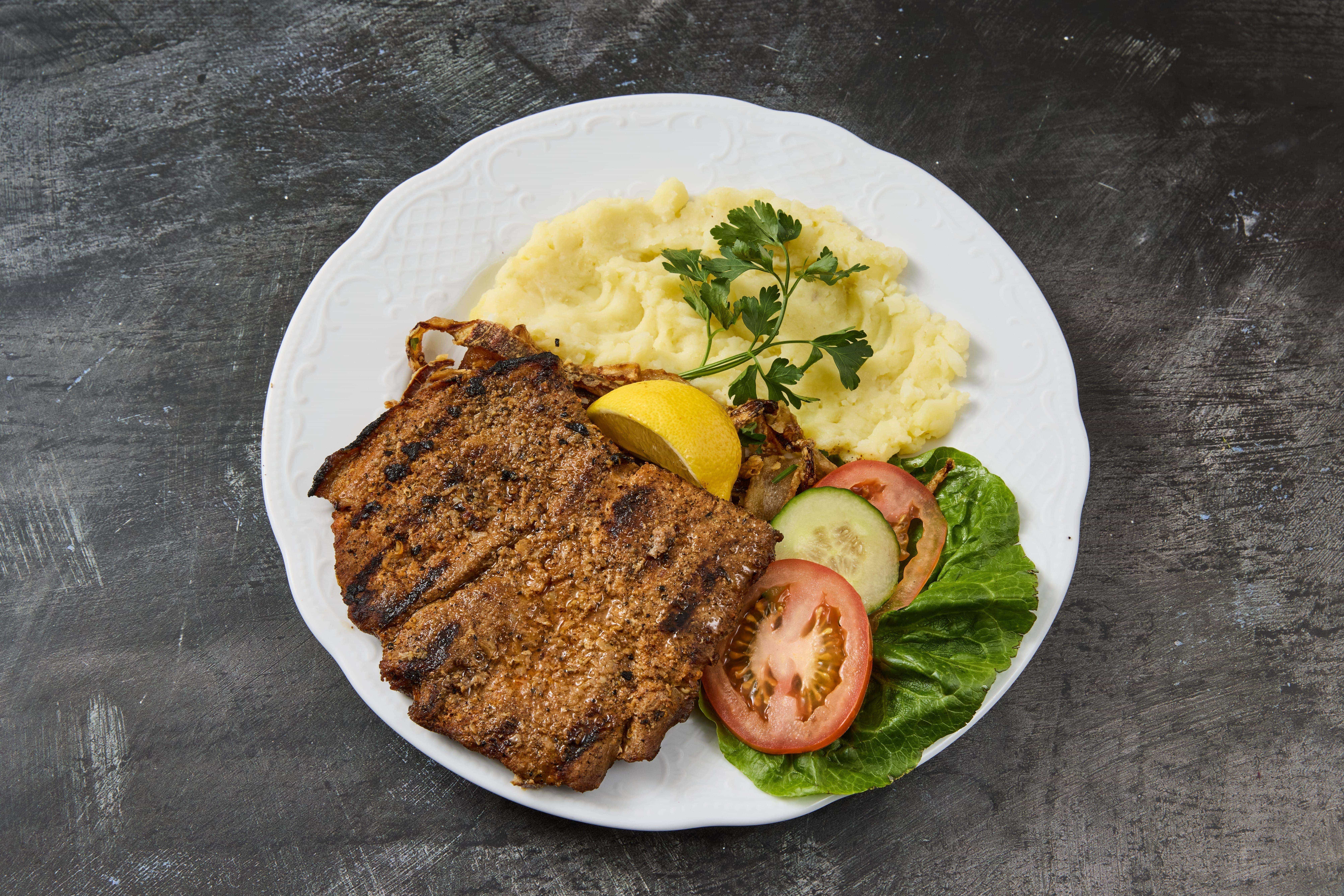 Schweinesteak Gegrilltes Schweinesteak mit Kartoffelpüree, frischem Gemüse und Zitrone – hausgemachtes Balkan-Essen zum Mitnehmen